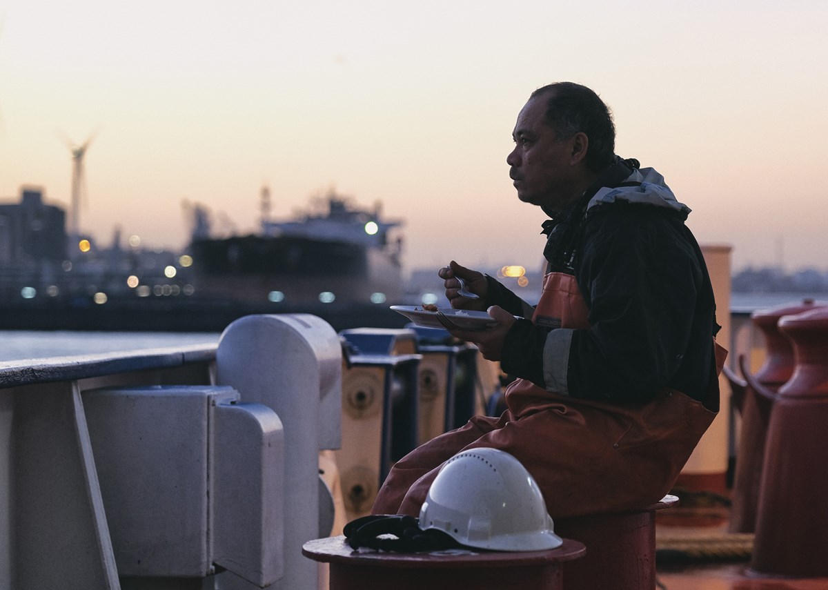 A man sitting on deck, eating and looking out with a dreamy gaze
