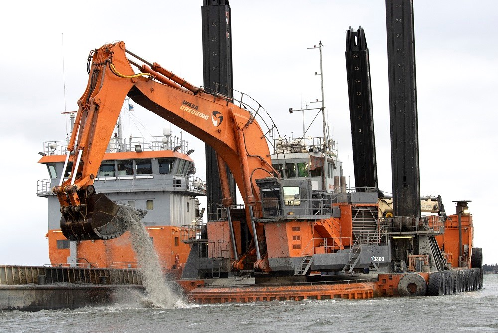 Med den här tekniken kommer sprängstenen att muddras. Bilden från muddringen av farleden till Hargs Hamn utanför Uppsala i höst. Foto: Agne Hörnestig. Muddringsverket i Hargs Hamn. En grävskopa hämtar upp muddermassa ur vattnet.