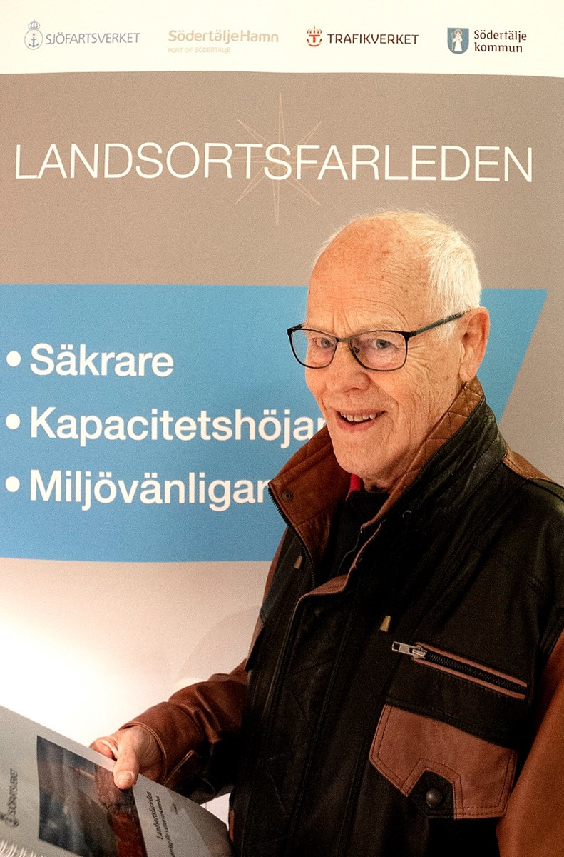 Bengt Haglund ser in i kameran och ler. I handen håller han en folder om Landsortsfarleden.