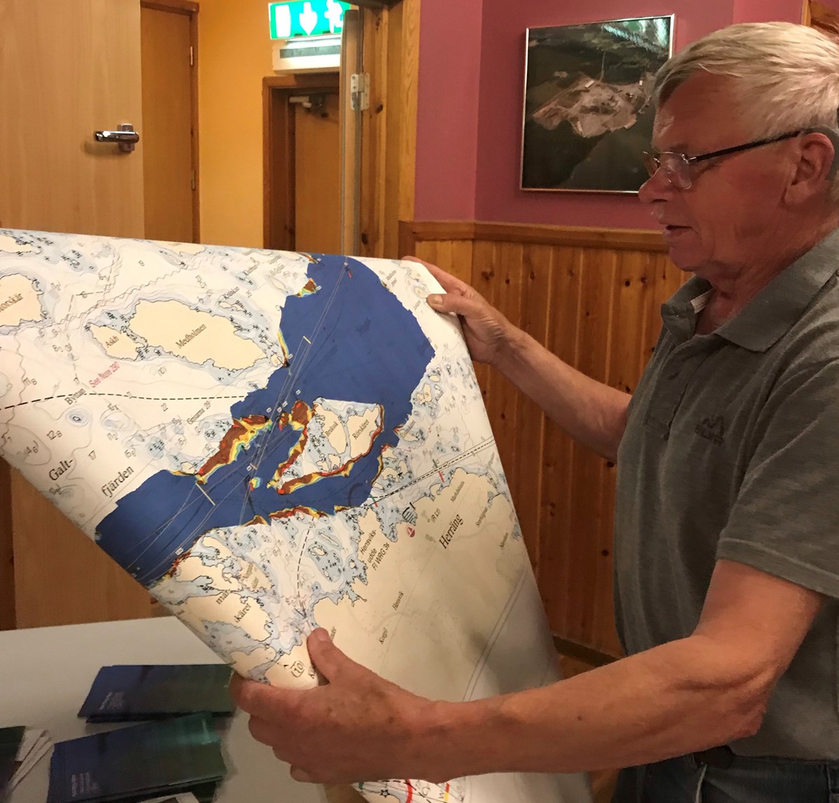 Lars-Erik Jansson, från Hargshamns båtklubb, var en av många som var extra intresserade av muddringsarbetet och ville veta mer om var, hur och när det kommer ske och hur det kommer påverka fisket och livet för de som bor i Hargshamn. Han fick med sig de tryckta sjökorten som visar var muddringen ska ske och även placering av sjösäkerhetsanordningarna. Foto: Annica Jonsson Lars-Erik håller upp ett sjökort för kameran som visar var muddringsarbetet ska göras.