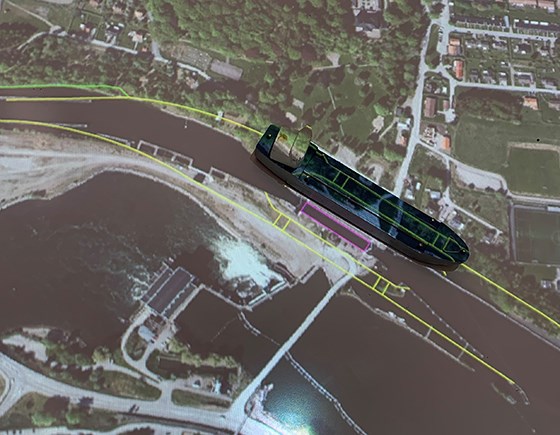 En modell av ett fartyg placeras (icke skalenligt) i den föreslagna sträckningen på kartan över Lilla Edets slussområde.