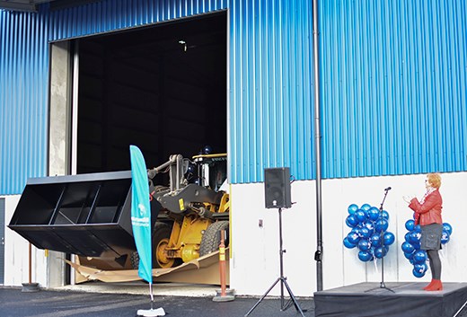 När det var dags att klippa bandet öppnades en av magasinets portar och en 21 ton tung hjullastare prydd med ballonger rullade igenom en avspärrning av papp. Till höger på bilden Elizabeth Salomonsson, kommunstyrelsens ordförande i Köpings kommun. Foto: Köping skommun Hjullastare invigde magasinsbyggnad.