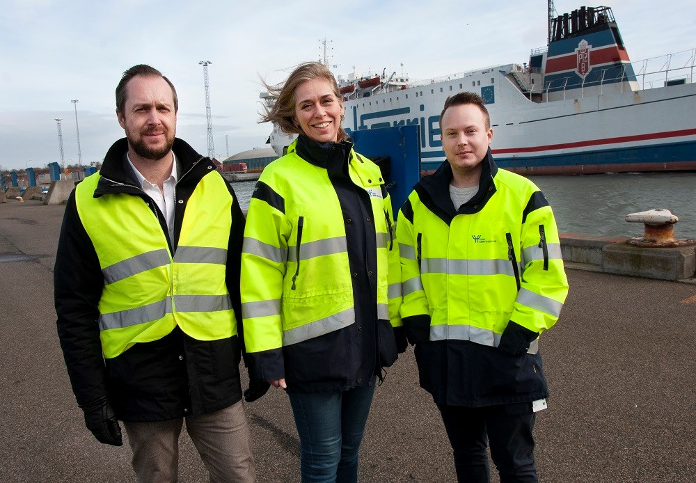 Friska vindar blåser in ännu mer framtidstro i Ystad hamn. Från vänster Johan Wahlström, projektledare Sjöfartsverket, Cecilia Ejlertsson, miljöansvarig och Andreas Malmström, projektledare, båda Ystad hamn. Foto: Agne Hörnestig Johan Wahlström, Cecilia Ejlertsson och Andreas Malmström står utomhus. Det blåser, de har gula rexlexvästar eller jackor på sig, ser in i kameran och ler. Bakom syns ett fartyg.