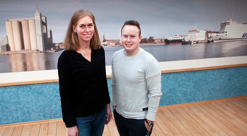Cecilia Ejlertsson och Andreas Malmström står inomhus framför en bild av hamnen. De ser in i kameran och ler.
