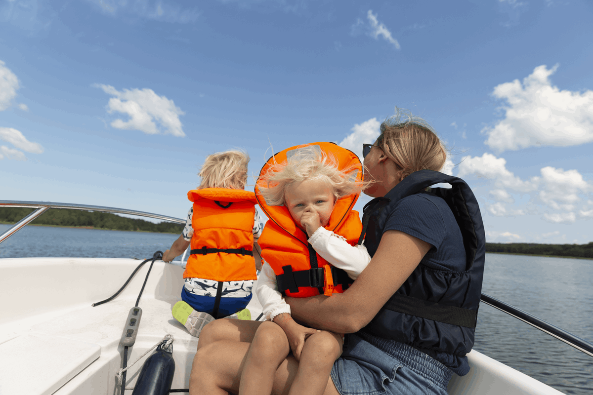 Bild på familj som åker båt, kvinna med två barn som har flytväst