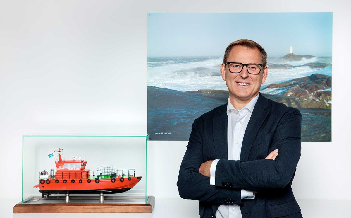 Porträtt på Erik Eklund som står framför en tavla med en lotsbåt i modell bredvid Porträtt på Erik Eklund som står framför en tavla med en lotsbåt i modell bredvid