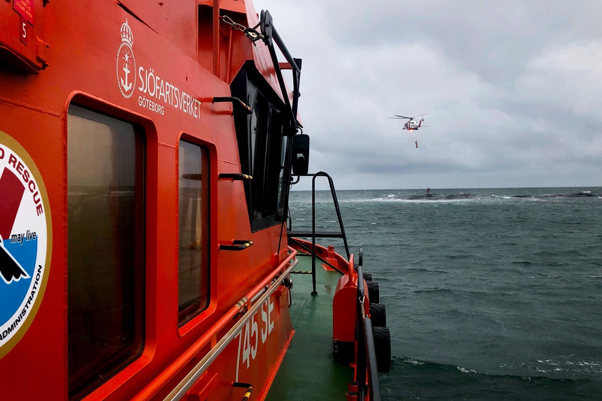 Sjöfartsverkets helikoptern från Säve vinschar upp de två nödställda från klipporna. Foto: Anton Stenros, båtman En lotsbåt syns till vänster. Till höger över havet flyger en helikopter.