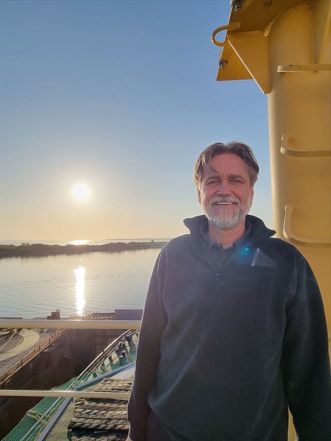Bild på Göran som står vid Frej med solnedgång i bakgrunden