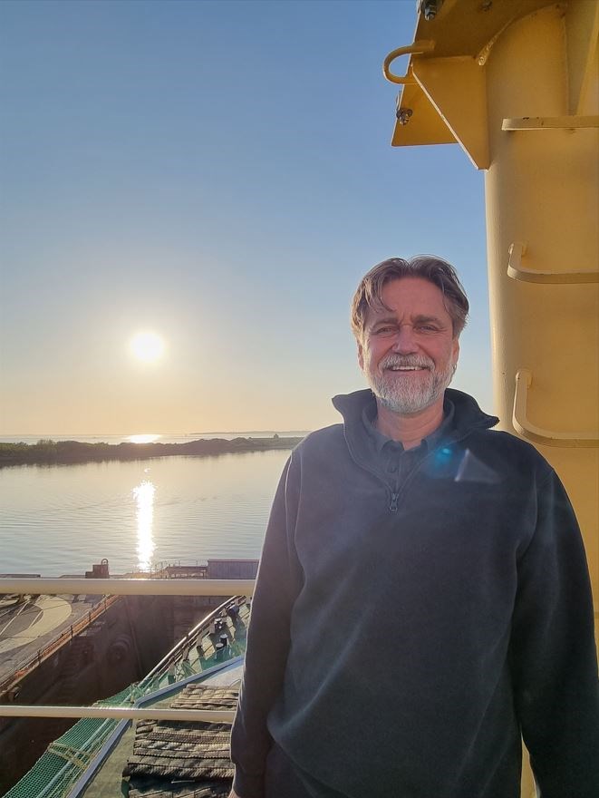 Göran Forss står och njuter av kvällssolen. Bild på Göran som står vid Frej med solnedgång i bakgrunden