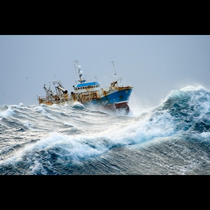 "I stormvejr" av  Guðmundur Guðmundsson. Rostigt fartyg seglar genom stora vågor.