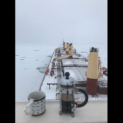 "Iskaffe"  av Jan Richard. Bild tagen från bryggan. Kaffepress och kaffekopp i förgrunden. Båten i vinterklimat i bakgrunden.