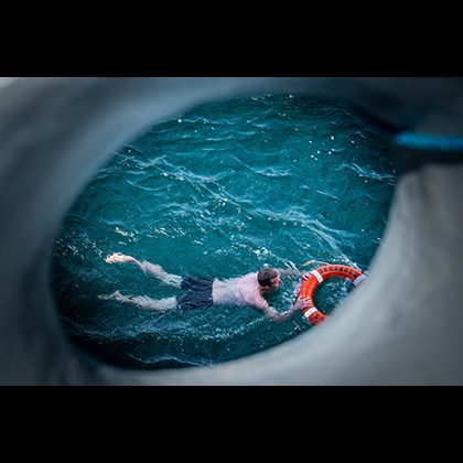 "Passing by" av Dan Deshayes,Man simmar med livboj. Bilden tagen genom ett tamåhål från ett fartyg.