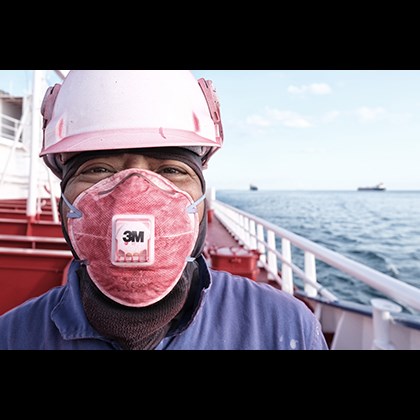 In the foreground a happy seafarer with a breathing mask full of red paint. Behind him, his vessel and the sea with two other vessels on the horizon.