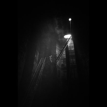 A man walking up the stairs in a dark tank space, with only light shining down from a hatch above