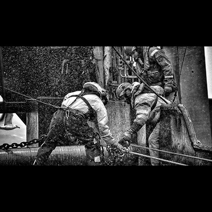 Nordic H.M - "Farligt arbeid” - Kristján Birgisson, IS Black and white photo of fishermen in stormy weather handling anchor chain while attached to safety ropes
