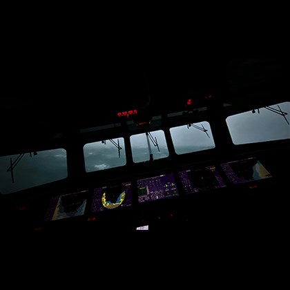 Photo taken from inside the bridge of a vessel, showing the control panel diagonally to the stormy sea outside