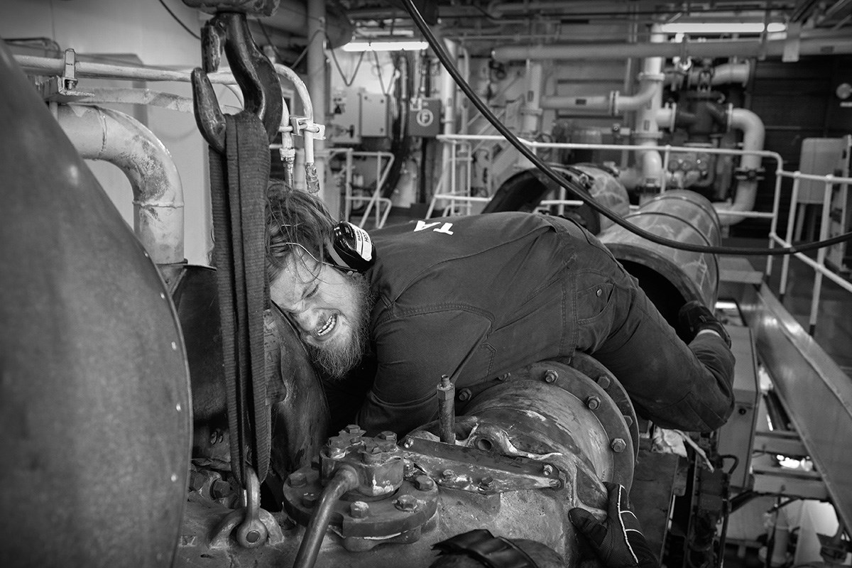 B/W photo of a mechanic trying to reach something in the machine