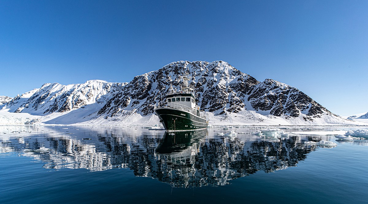 Fartyg speglas i vatten i polarmiljö