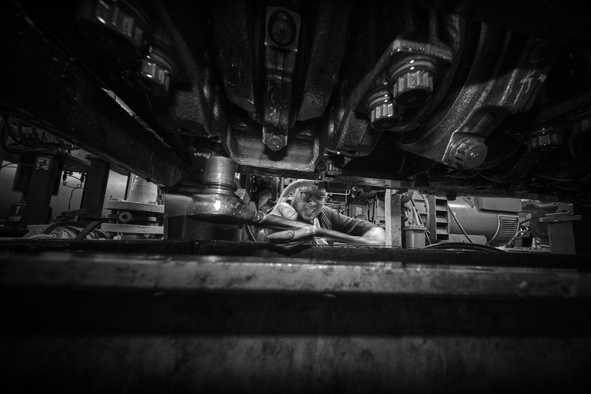 Black and white photo of a man with a wrench, trying to fit it on a bolt