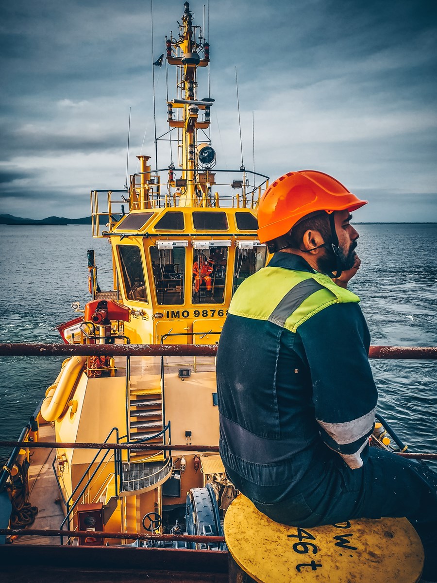 A seafarer in orange helmet sitting and contemplating while looking out at sea