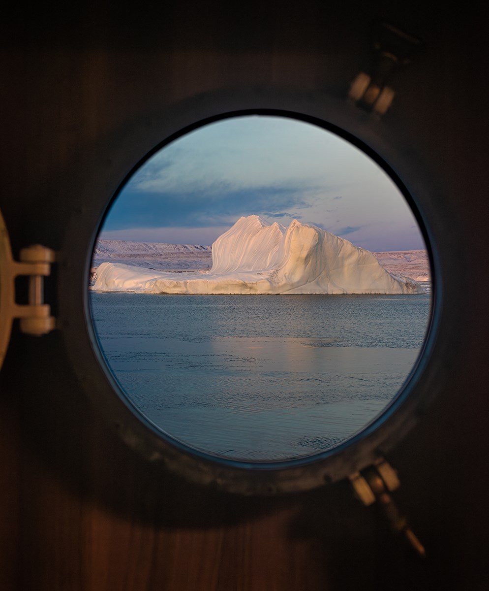 An iceberg is visible through the ship's porthole