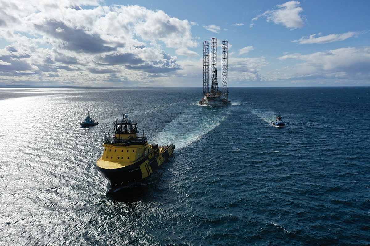 A ship is towing a rig and is flanked by two smaller ships
