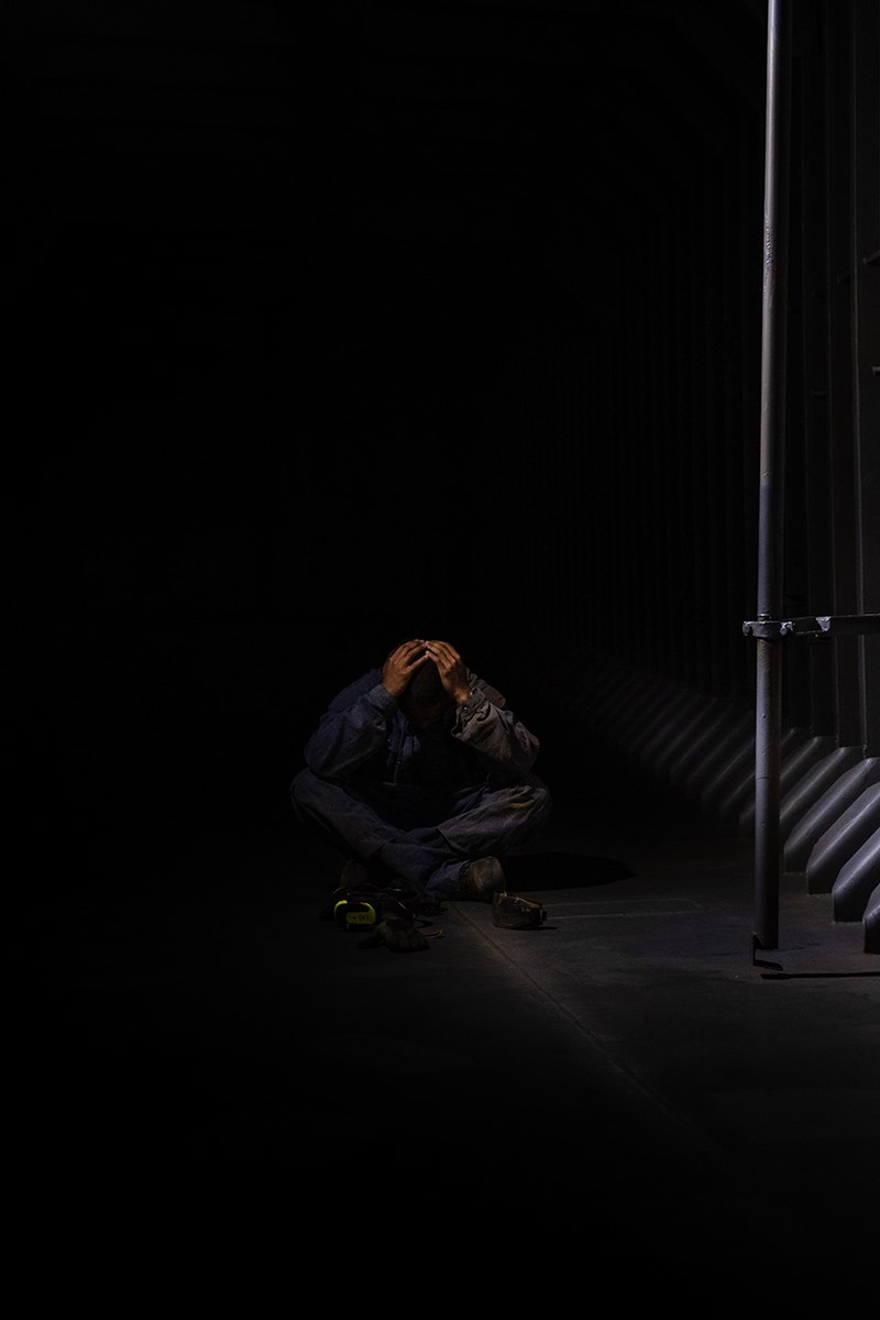 A person is sitting in a dark space, holding his head