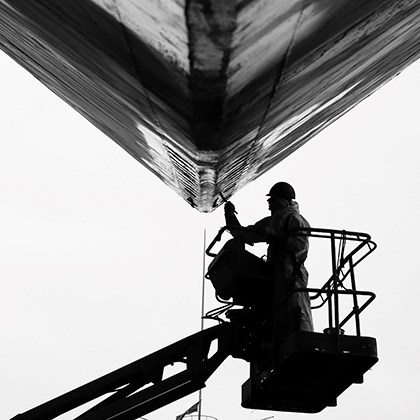 Black and white photo of a man painting load line markings on a vessel