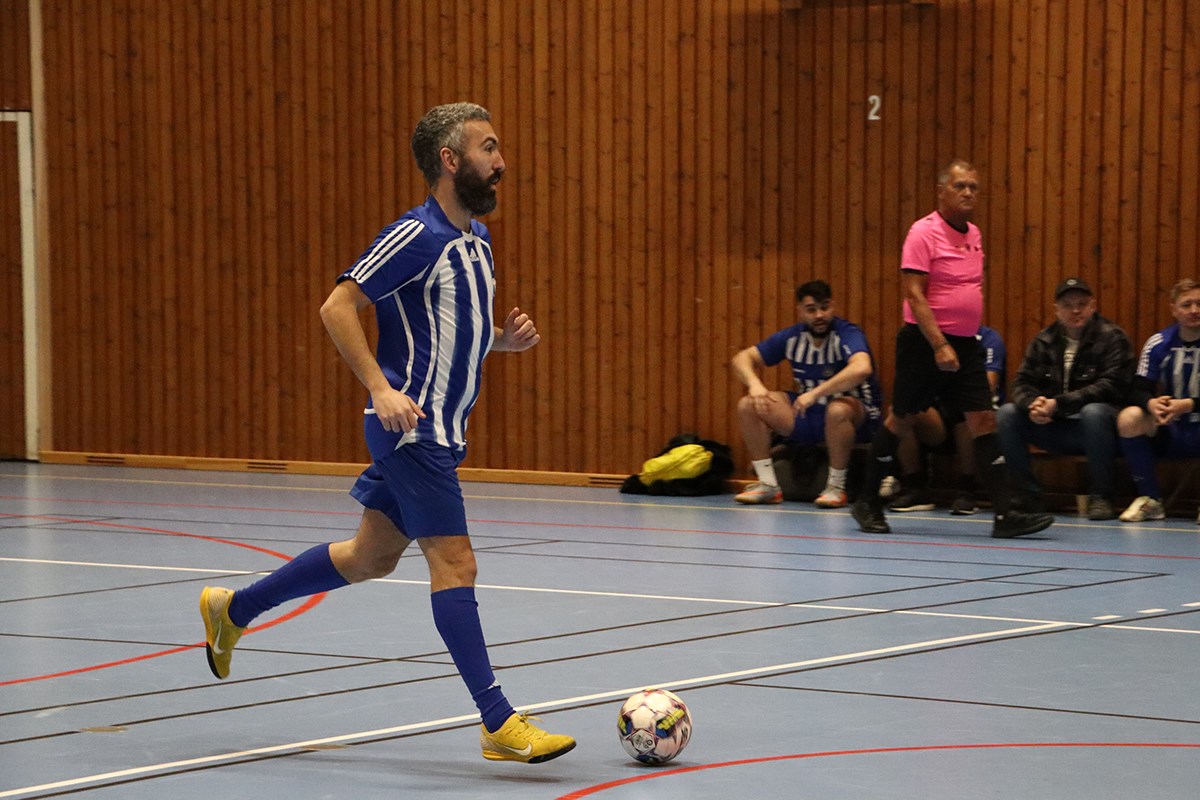 En inomhusfotbollsspelare springer med bollen. I bakgrunden syns avbytarbänken och domaren