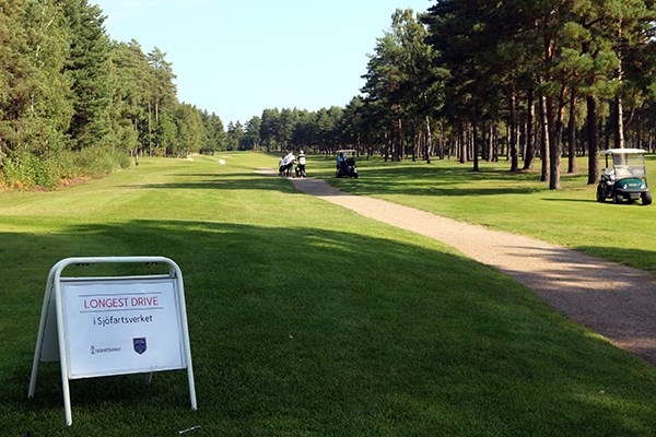 Golfbana. I förgrunden en skylt som säger "Longest drive". I bakgrunden skymtas golfspelare