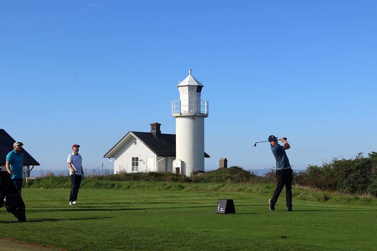 Tre golfspelare i bild, i bakgrunden (i mitten) syns en vit fyr. Tre golfspelare i bild, i bakgrunden (i mitten) syns en vit fyr.