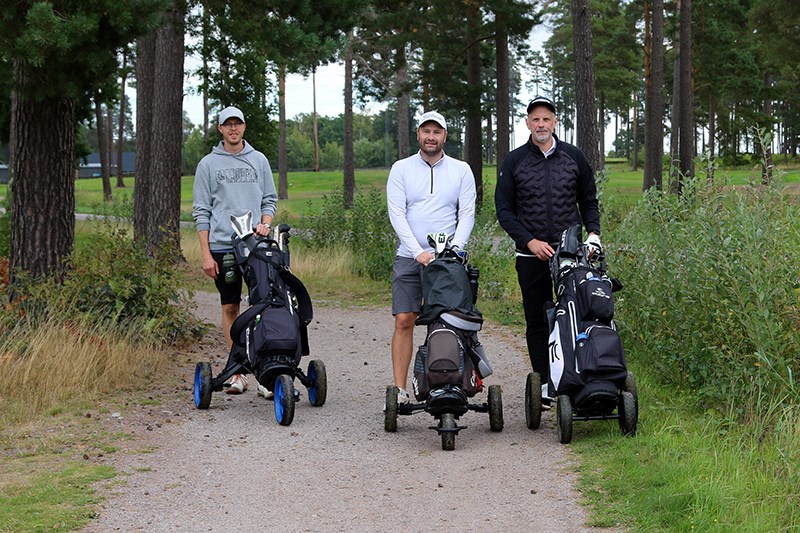 Tre golfspelare går på grusväg med sina golfvagnar