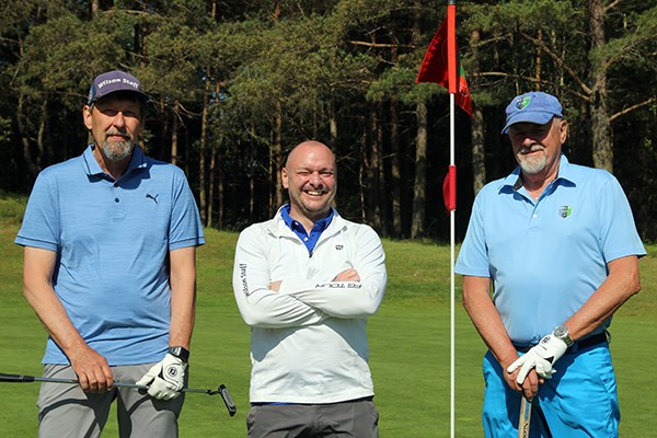 Tre golfspelare poserar vid hålflaggan.