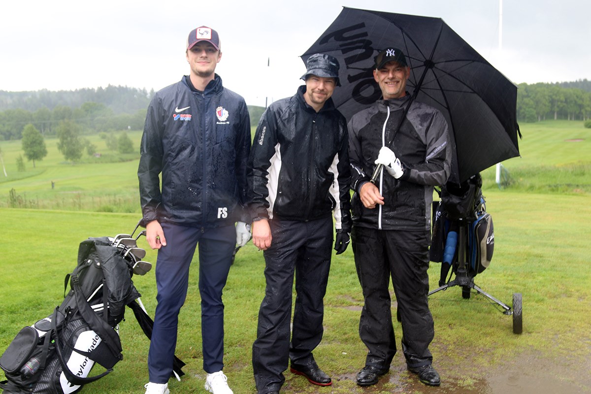 Tre golfspelare under paraply