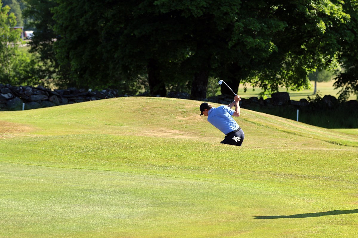 Man i blå skjorta och keps slår iväg en golfboll