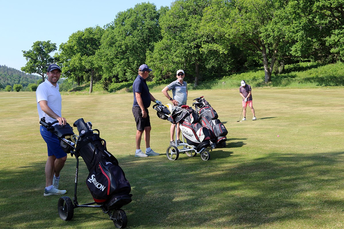 Tre spelare vid sina golfbagar medan den fjärde slår