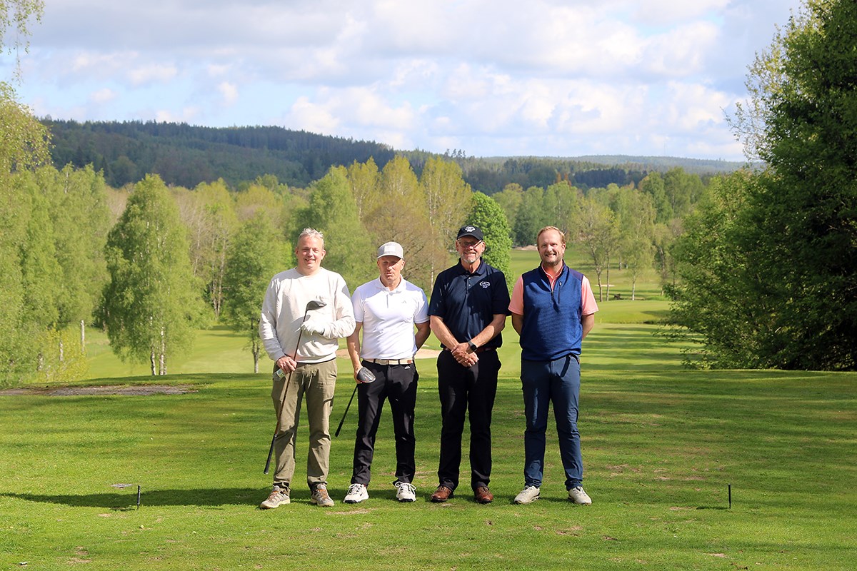 Fyra golfspelare har stannat upp i spelet och poserar. Vackra gröna vyer i bakgrunden