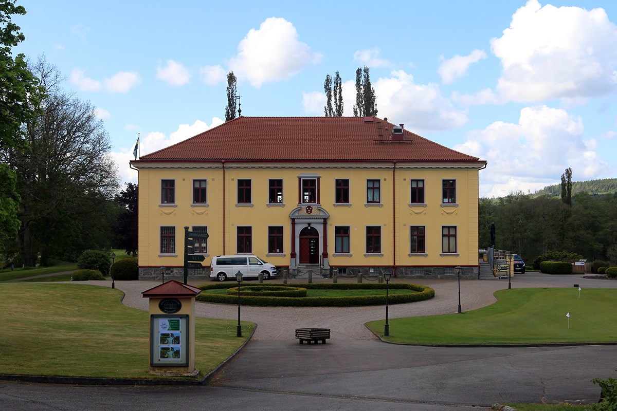 En gul herrgård med tegelfärgat tak. Framför den en grönskande rondell i den krattade grusgången