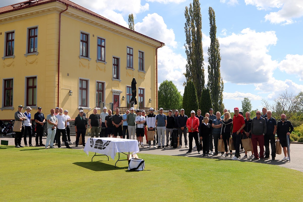 En stor grupp golfspelare står uppställda framför en gul herrgårdsbyggnad
