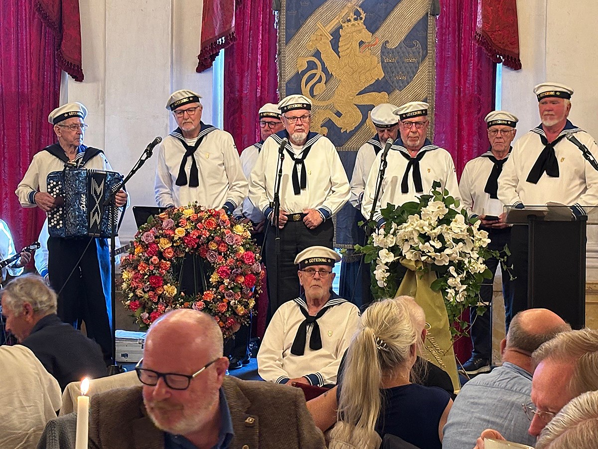 Flottans män underhåller till kaffet, som avslutar högtiden. Åtta personer i sjömanskostymer och -mössor står på scenen och underhåller. I förgrunden ses några av åhörarna fika
